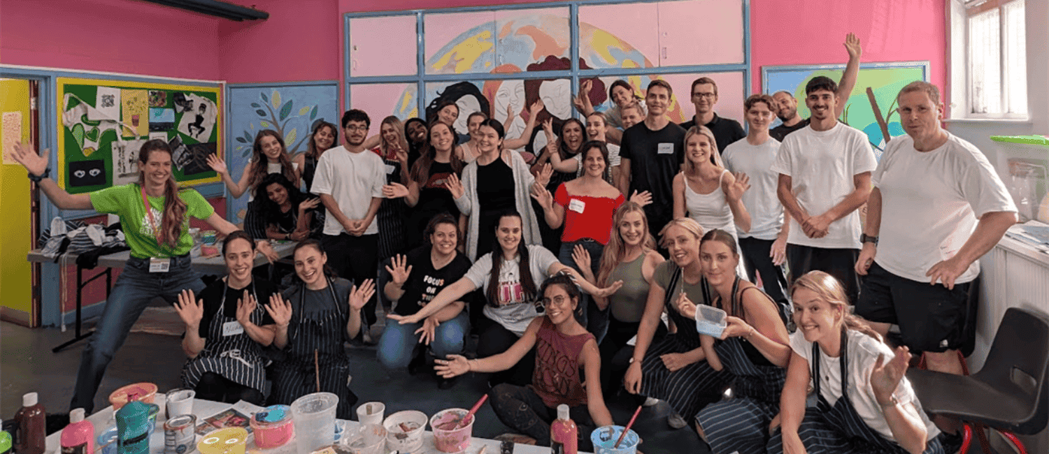 Large group of employees volunteering together in 2024, smiling and posing in front of a colourful mural