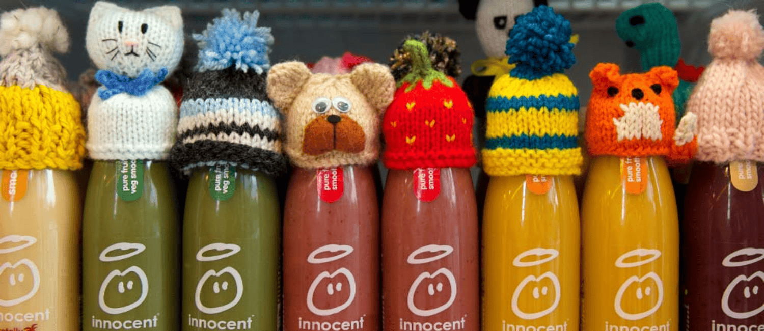 Row of Innocent smoothie bottles topped with colourful, hand-knitted hats in various playful designs as part of a charity campaign
