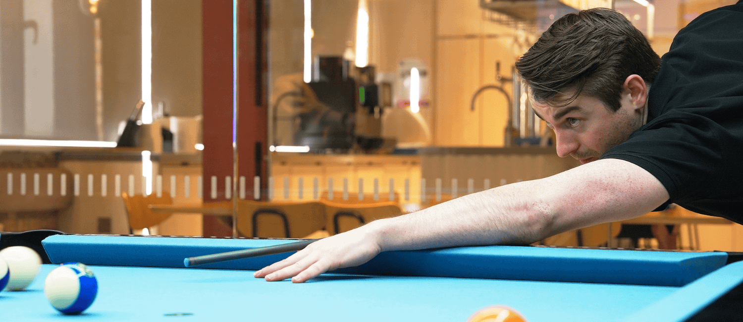 A young man, Robert Keys, focused as he lines up a shot while playing pool during the 1st Formations Pool Tournament.