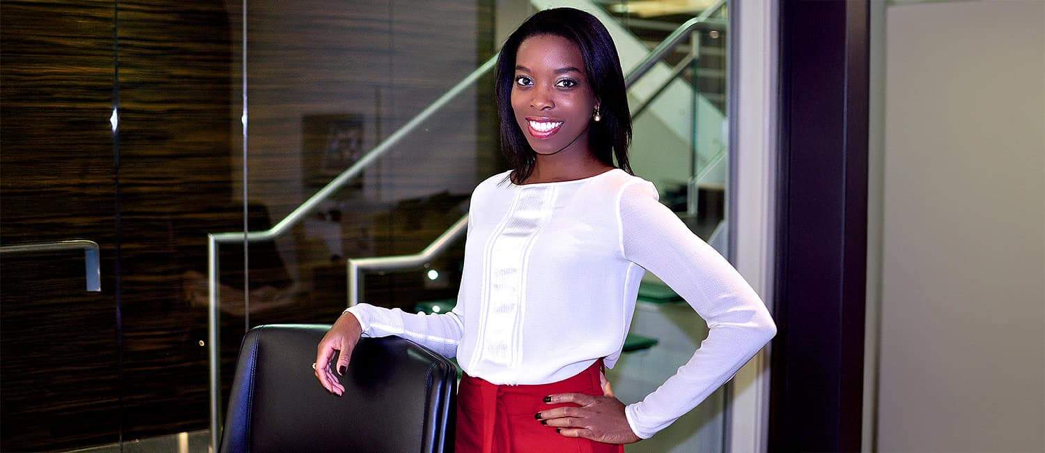 Ade Hassan MBE, founder of Nubian Skin, a Black-owned inclusive lingerie brand, stands confidently in a modern office space, wearing a white top and red trousers