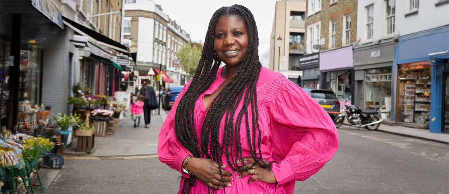 Charlotte Mensah, founder of Hair Lounge, a Black-owned hairdressing salon and hair care product brand, poses confidently on a London street in a bright pink outfit