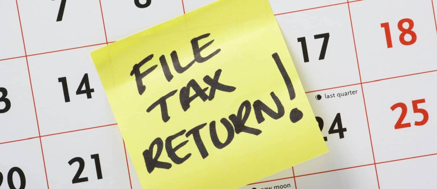 Image of a calendar with a yellow Post-It note attached and 'File Tax Return!' written on it