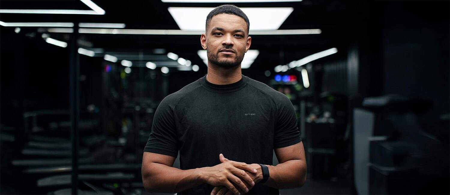Steven Bartlett, Co-Founder of thirdweb and Flight Story, stands confidently in a modern, dimly lit space with futuristic lighting. He is wearing a black t-shirt and a smartwatch, with his hands loosely clasped in front of him