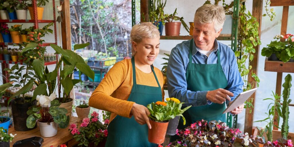 Two people wearing green aprons working together in a flower shop surrounded by plants, representing a family business in the gardening or floral industry