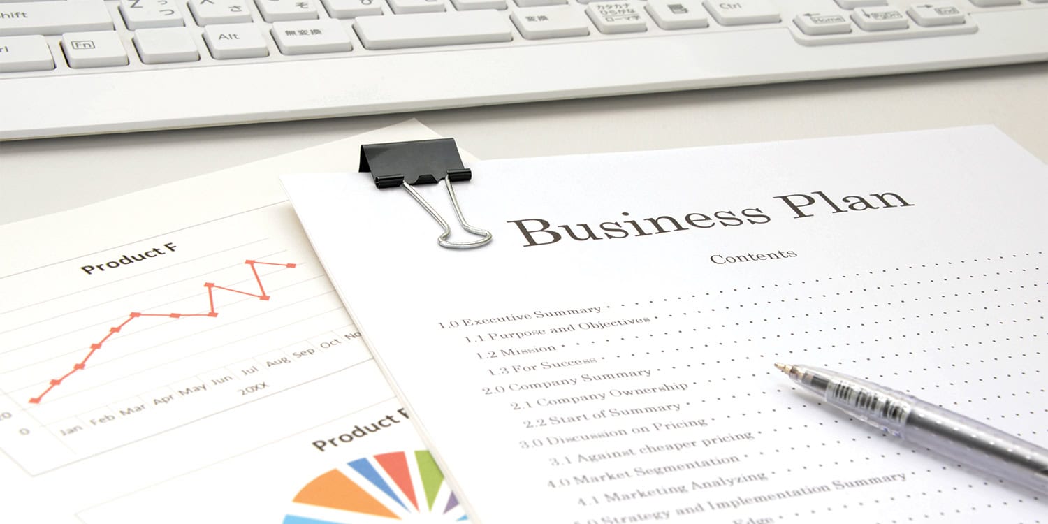 Business plan document on a desk beside sales charts and a keyboard, suggesting planning strategy.