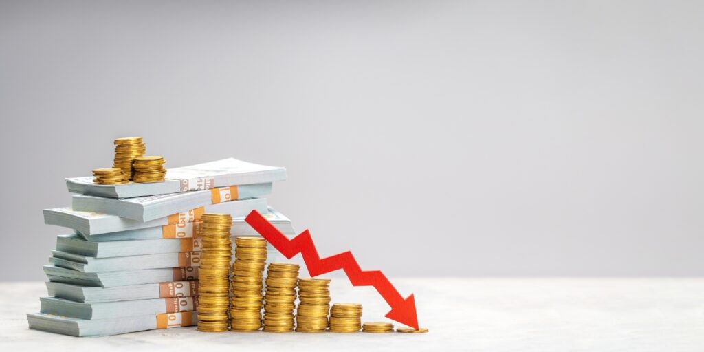 Stacks of money and coins with a red downward arrow showing financial decline.