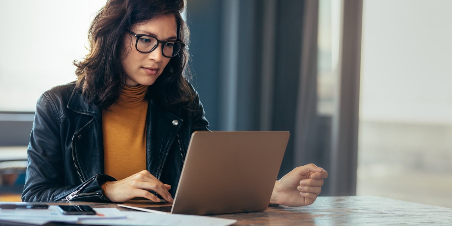 Young professional woman working on laptop in modern office, focused on remote work or online research
