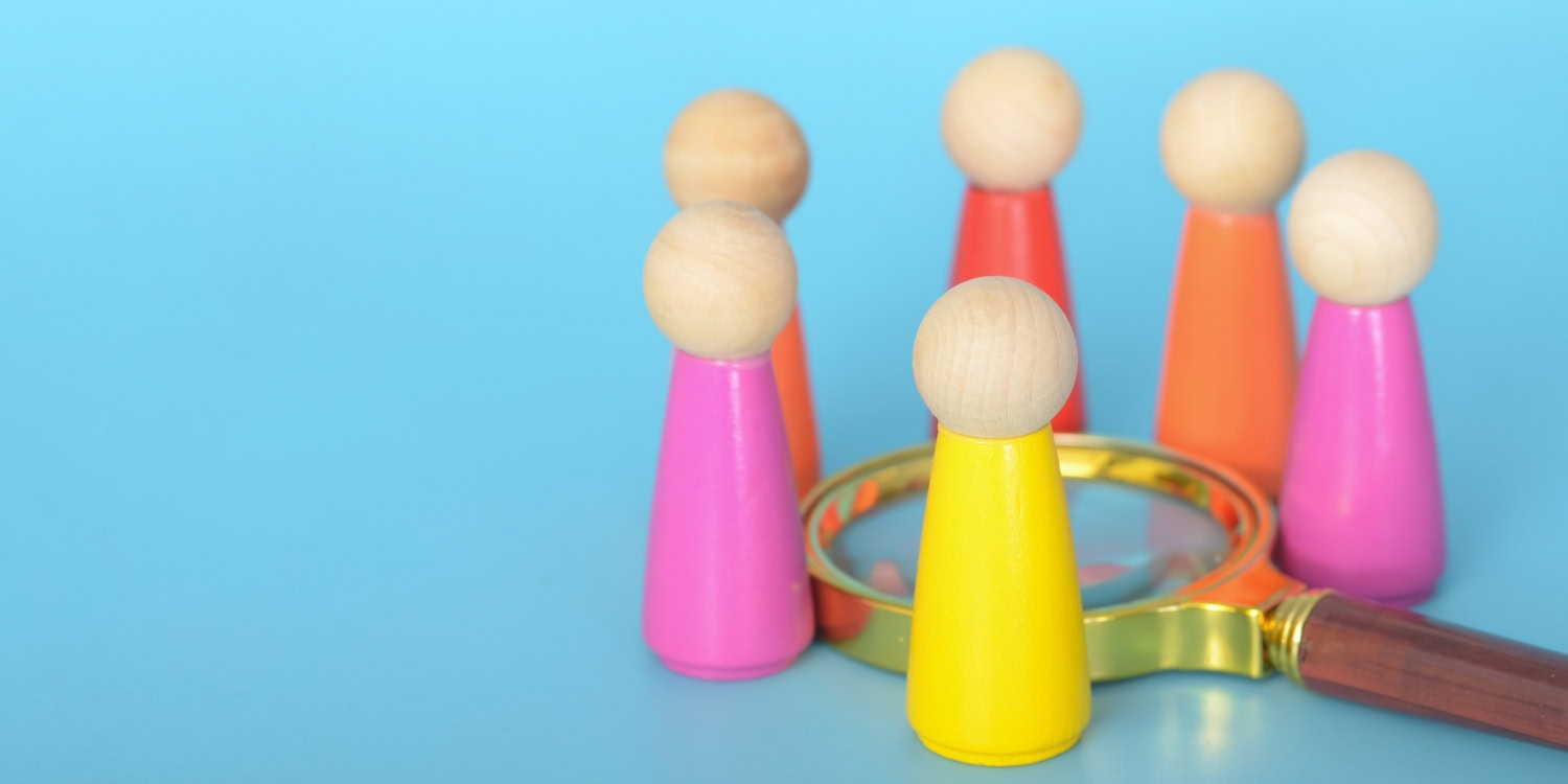 Magnifying glass identifying colourful wooden figures as relevant legal entities for the PSC register