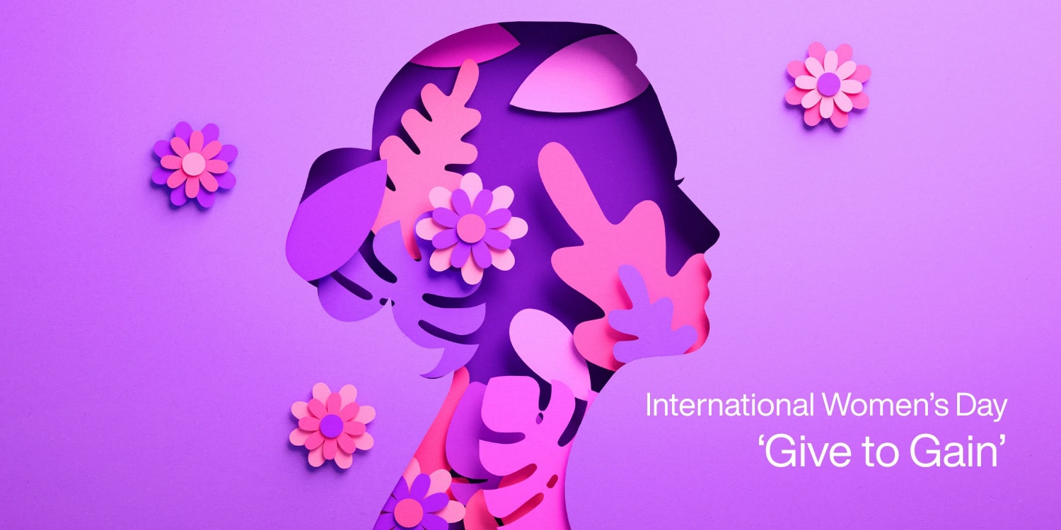 A purple background features a stylised silhouette of a woman's profile surrounded by colourful paper flowers and leaves. The text reads "International Women’s Day 'Give to Gain'