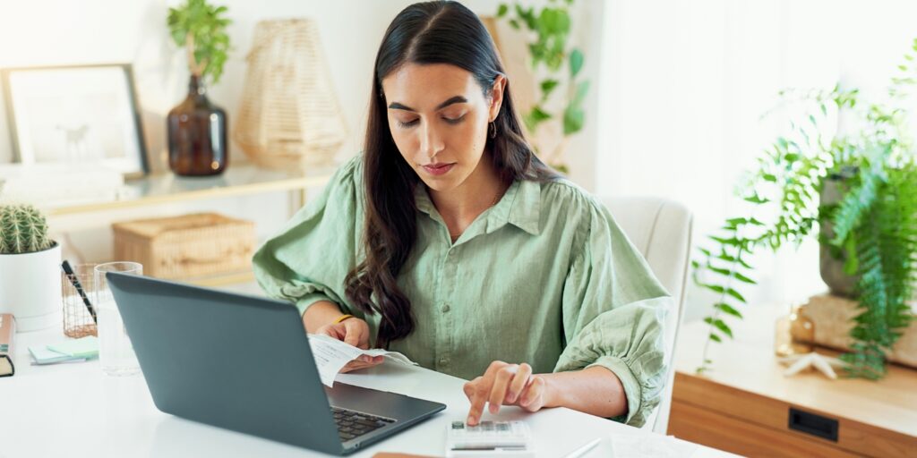 Woman reviewing bills and using a calculator at a desk to determine costs of keeping her company dormant.
