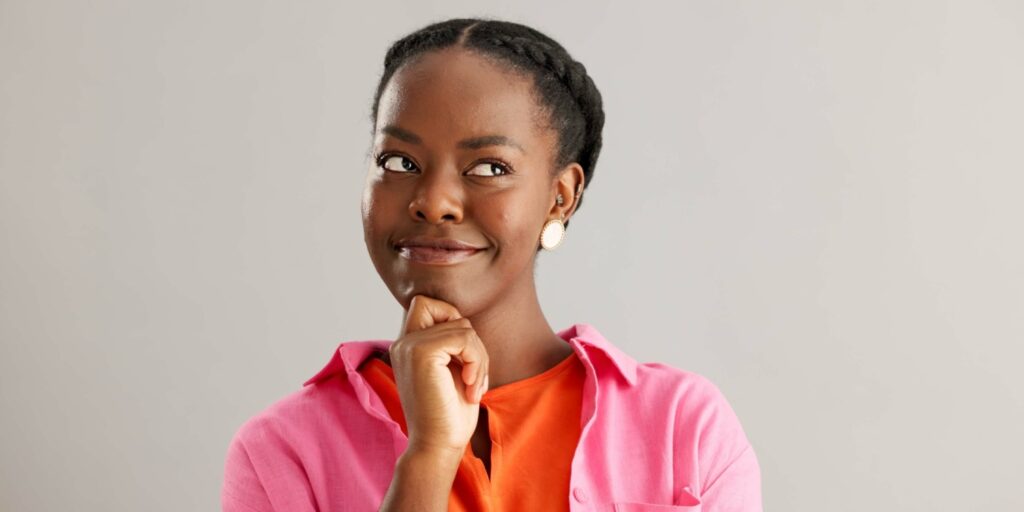 A young woman resting her chin on her hand and looking upward thoughtfully, wearing a pink shirt, considering starting a business under 18