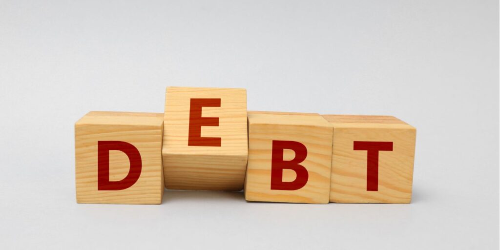 Wooden blocks arranged in a row, spelling the word 'DEBT' in red letters.