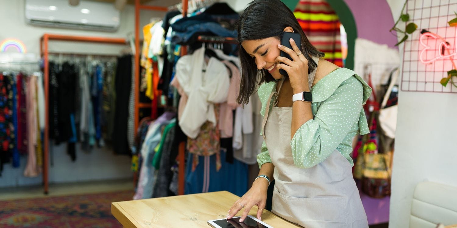 A retailer worker standing behind a desk, taking a call and looking at an iPad.