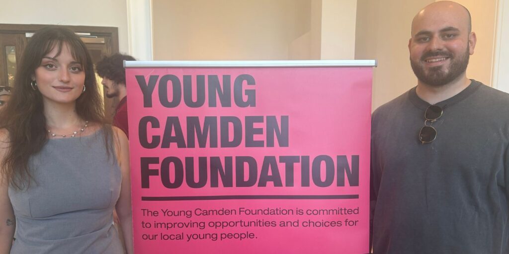 Two members of the 1st Formations team standing either side of a pink sign that reads 'YOUNG CAMDEN FOUNDATION'.