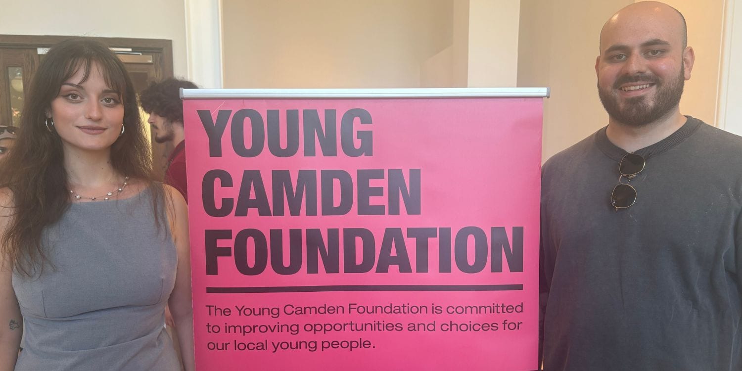 Two members of the 1st Formations team standing either side of a pink sign that reads 'YOUNG CAMDEN FOUNDATION'.