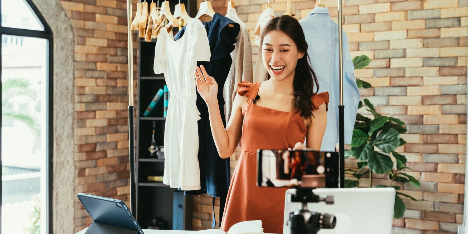 An influencer making a video of herself on her phone, showing clothes in the background.