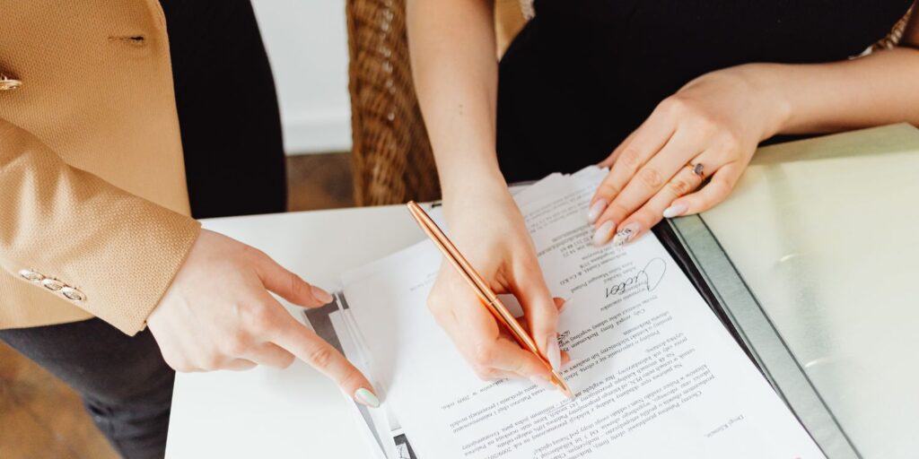 Two businesswomen signing a legal contract with a gold pen.