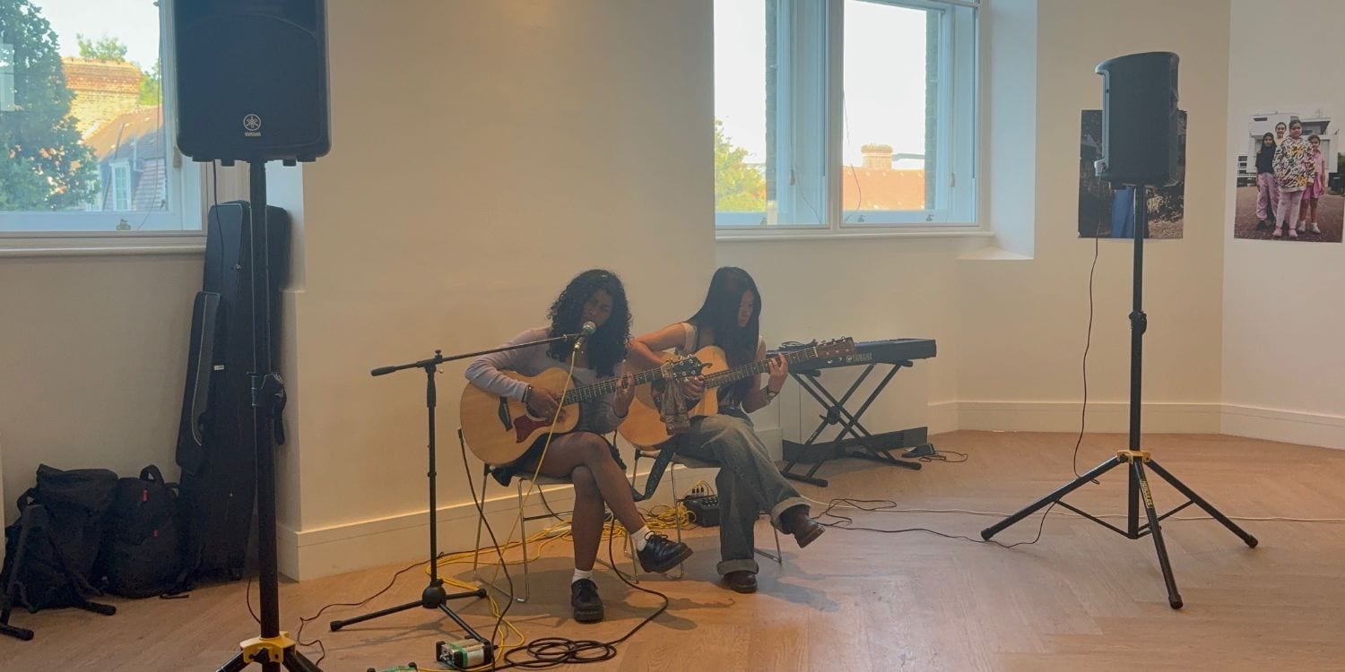Two people playing guitars and singing at the Young Camden Foundation summer party.